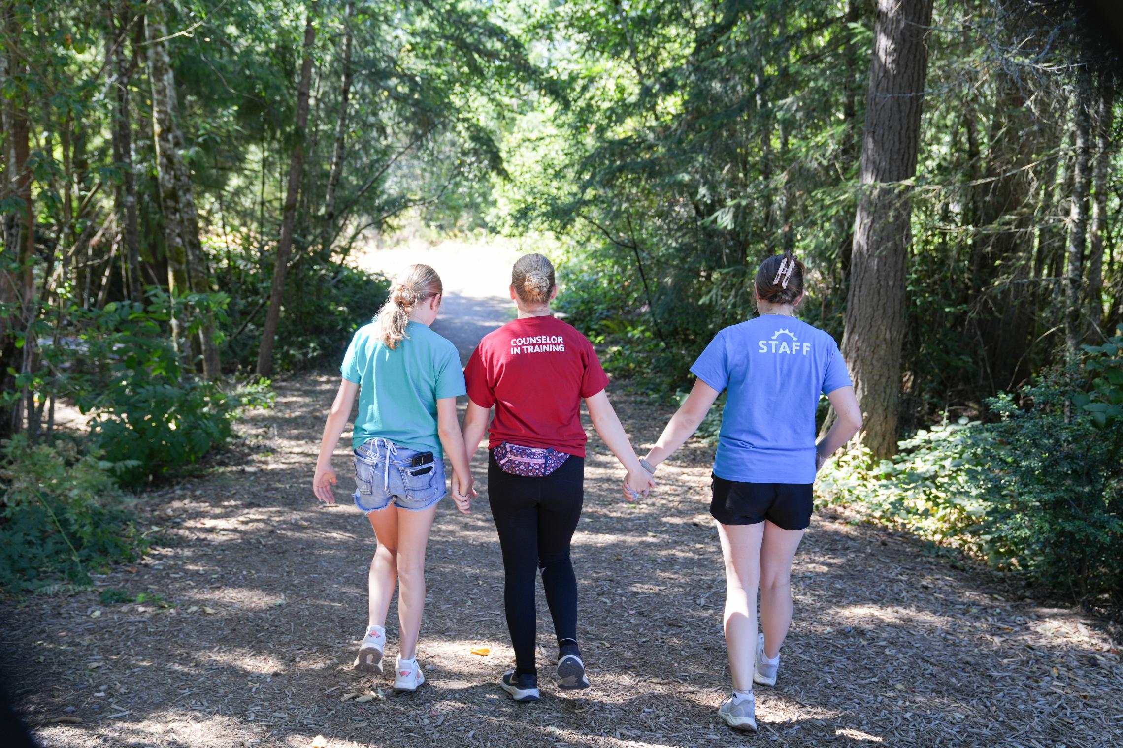 Three camp sisters walking away on a trail holding hands