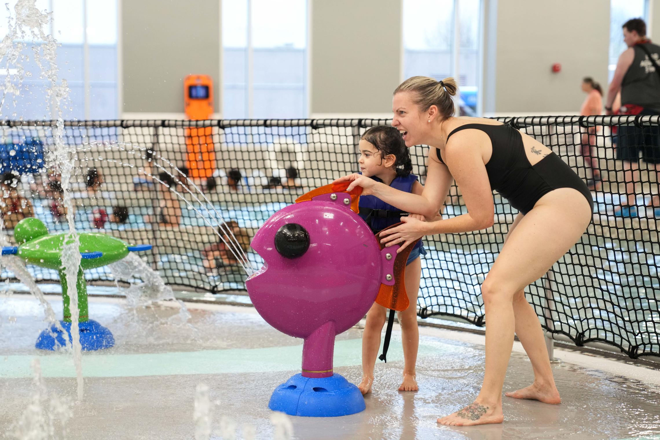 Adult and child enjoying a YMCA indoor splash pad and aquatic center, highlighting family swim, water safety, and summer recreation in Pierce and Kitsap Counties.