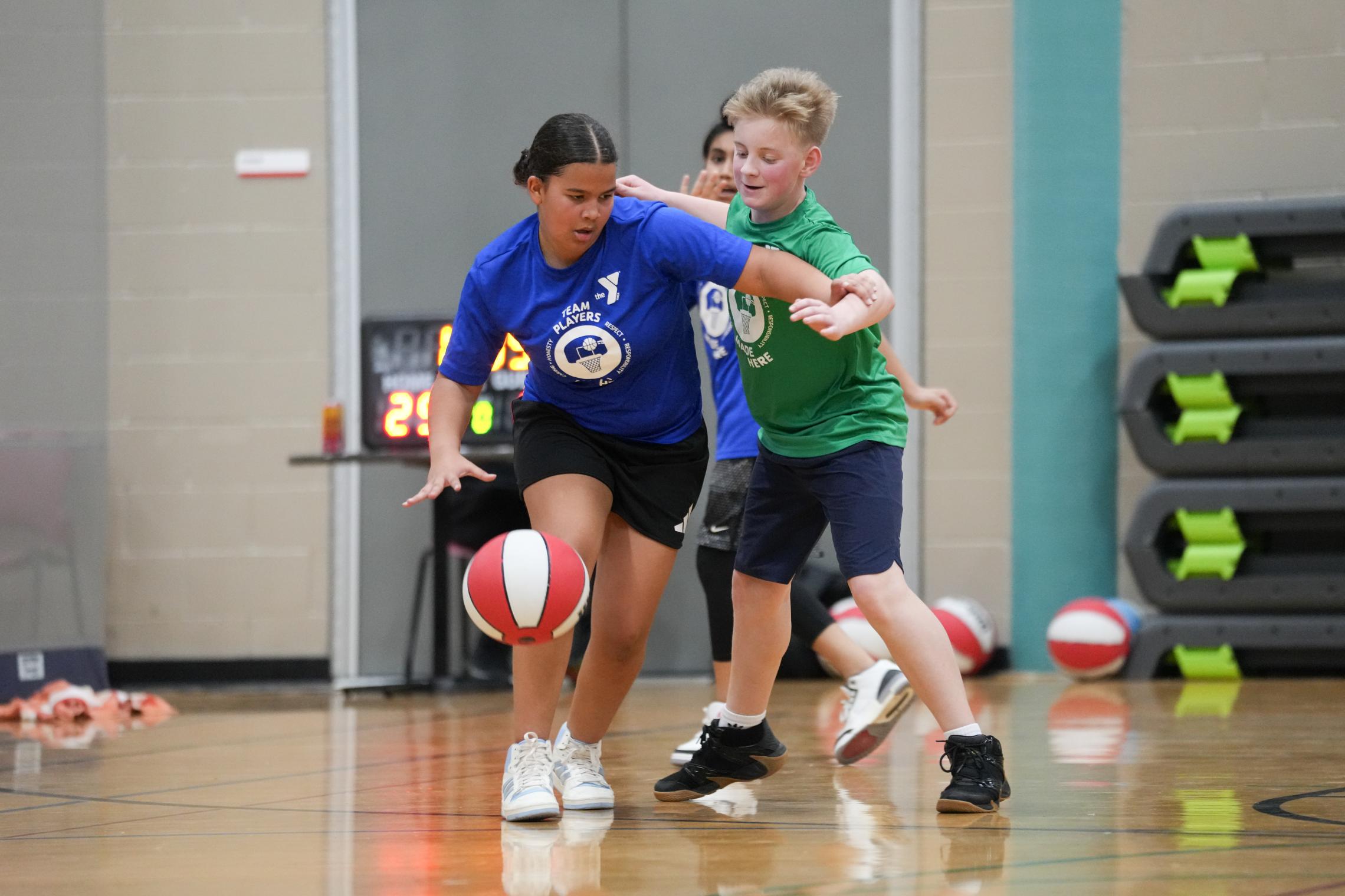 Youth participants playing basketball during a Mel Korum Family YMCA Youth Basketball League game on an indoor court.