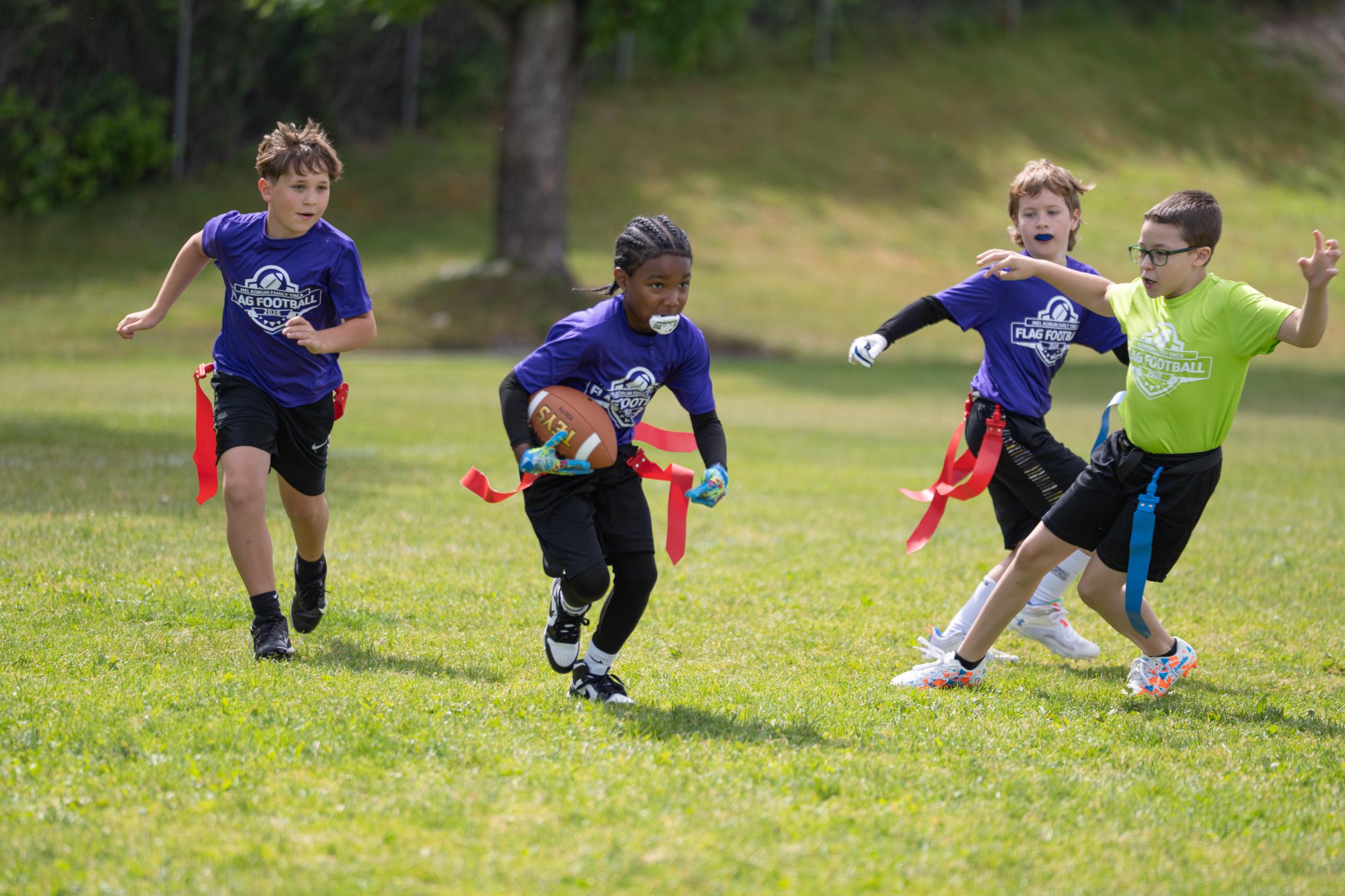 Youth athletes playing flag football during a Mel Korum Family YMCA youth flag football game on an outdoor field.