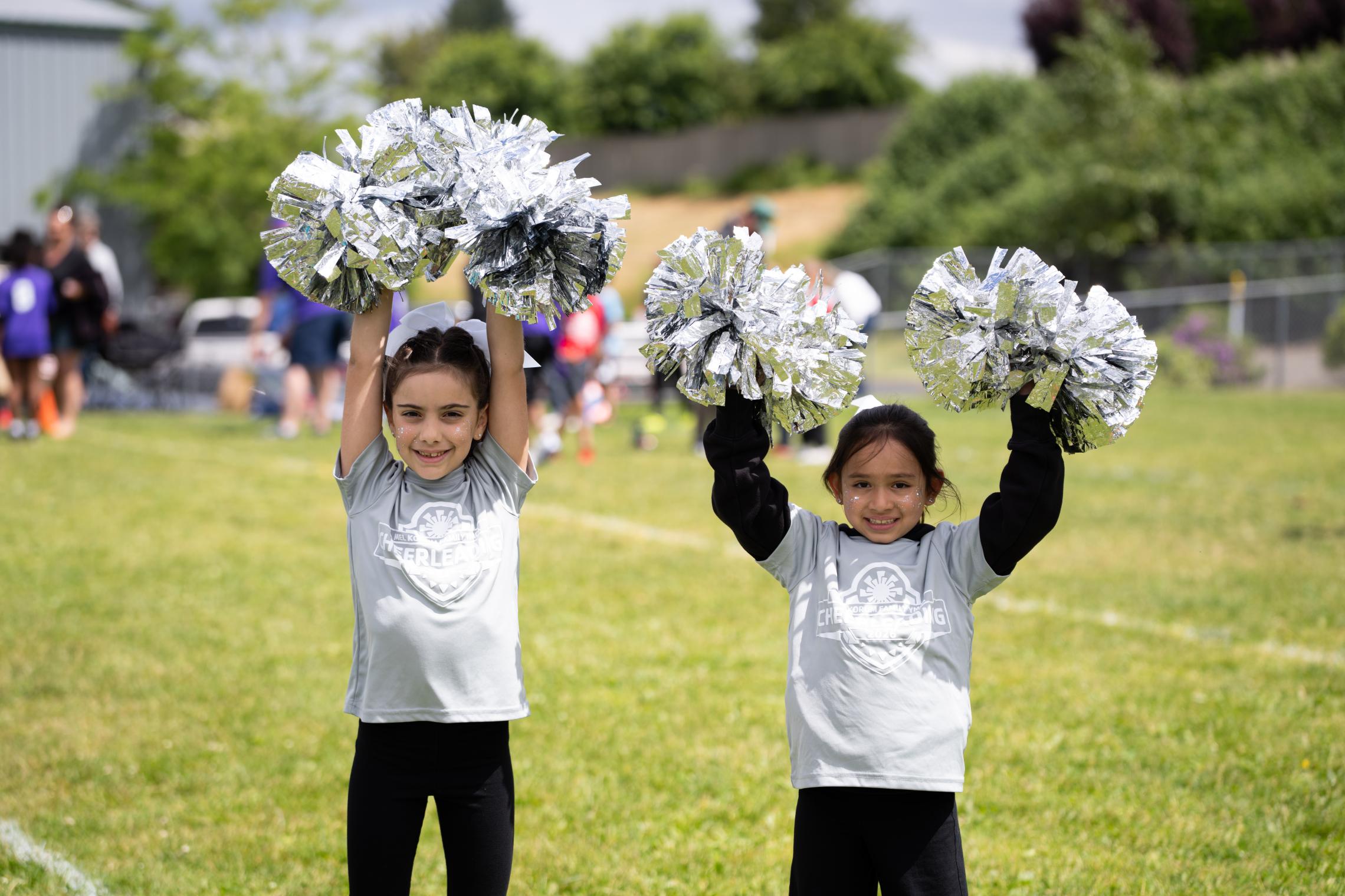 Youth cheerleaders participating in a Mel Korum Family YMCA cheerleading program during an outdoor youth sports event.
