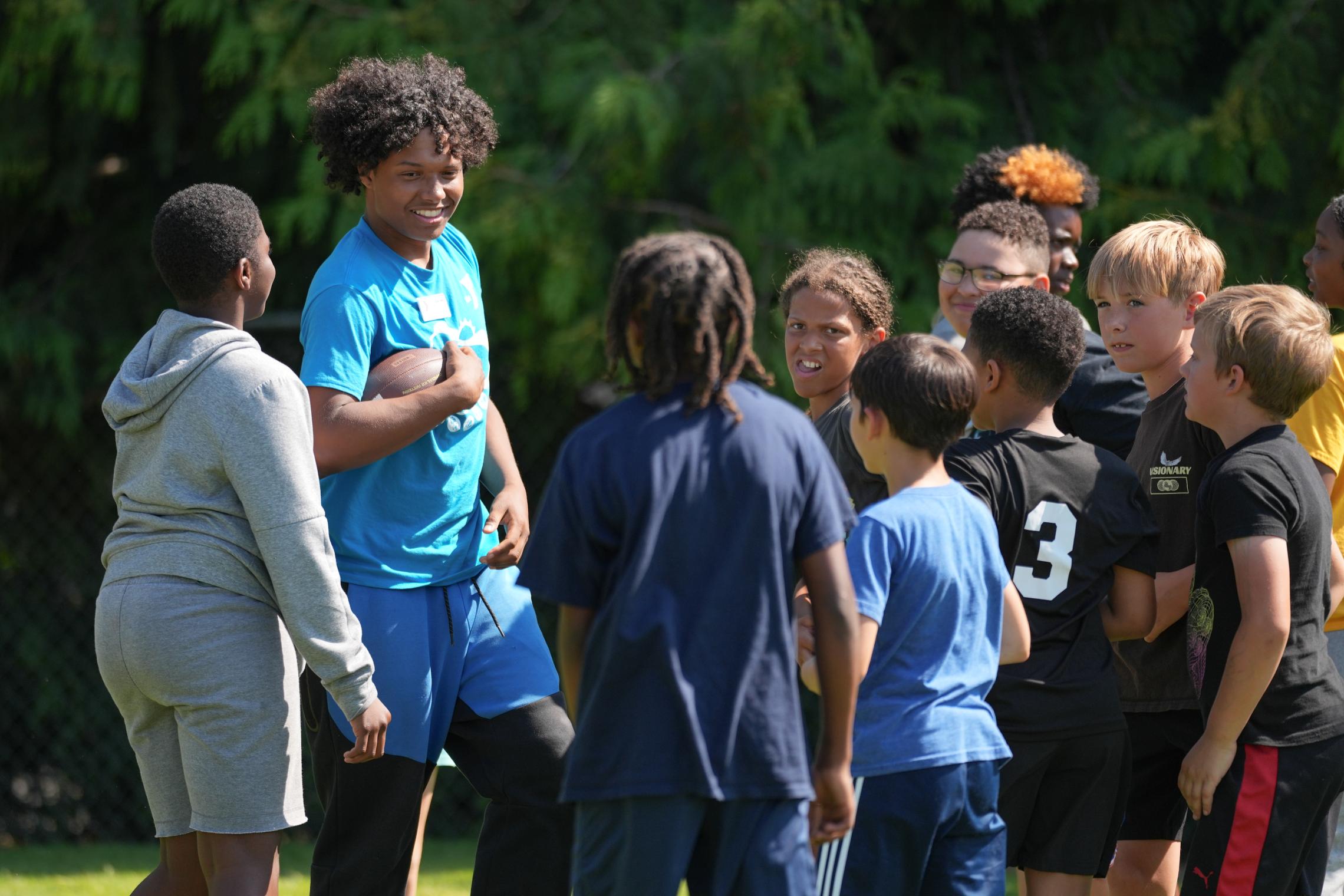 YMCA summer camp counselor leads a group of children in an outdoor team-building activity, encouraging participation, inclusion, and social development during summer camp.