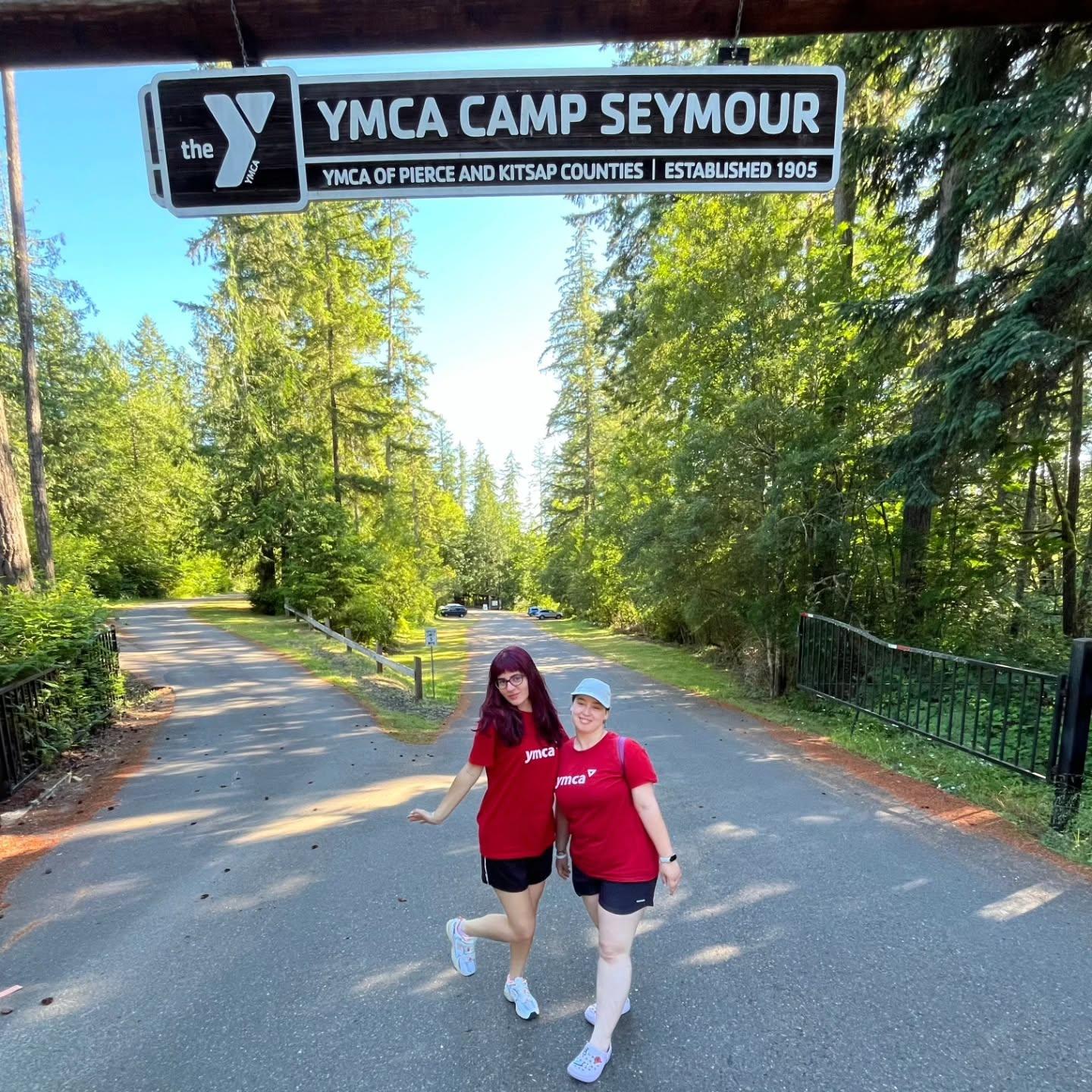 Two international staff members from Kosovo stand beneath the YMCA Camp Seymour entrance sign, representing cultural exchange, global leadership, and international camp staff in Washington State.