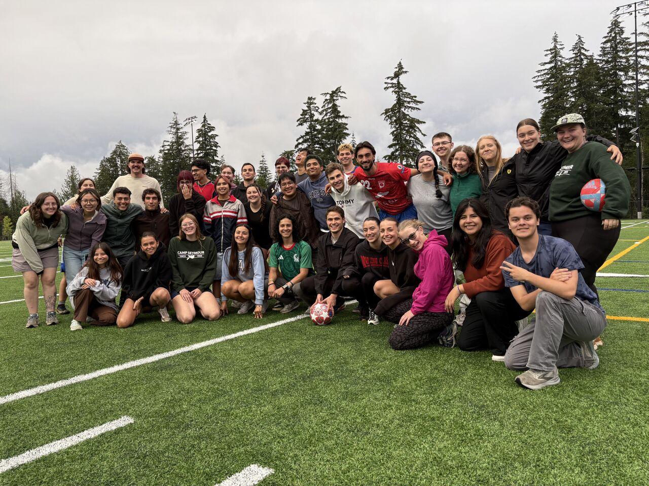 International staff from around the world gather at the Gig Harbor Sports Fields after a soccer match, celebrating cultural exchange, teamwork, and community at YMCA Camp Seymour.