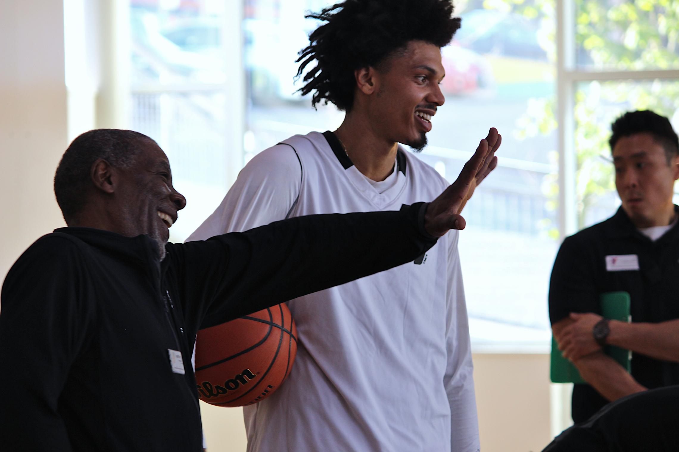 Two participants stand near a basketball court at the University YMCA Student Center, with one holding a basketball while speaking with others gathered nearby.