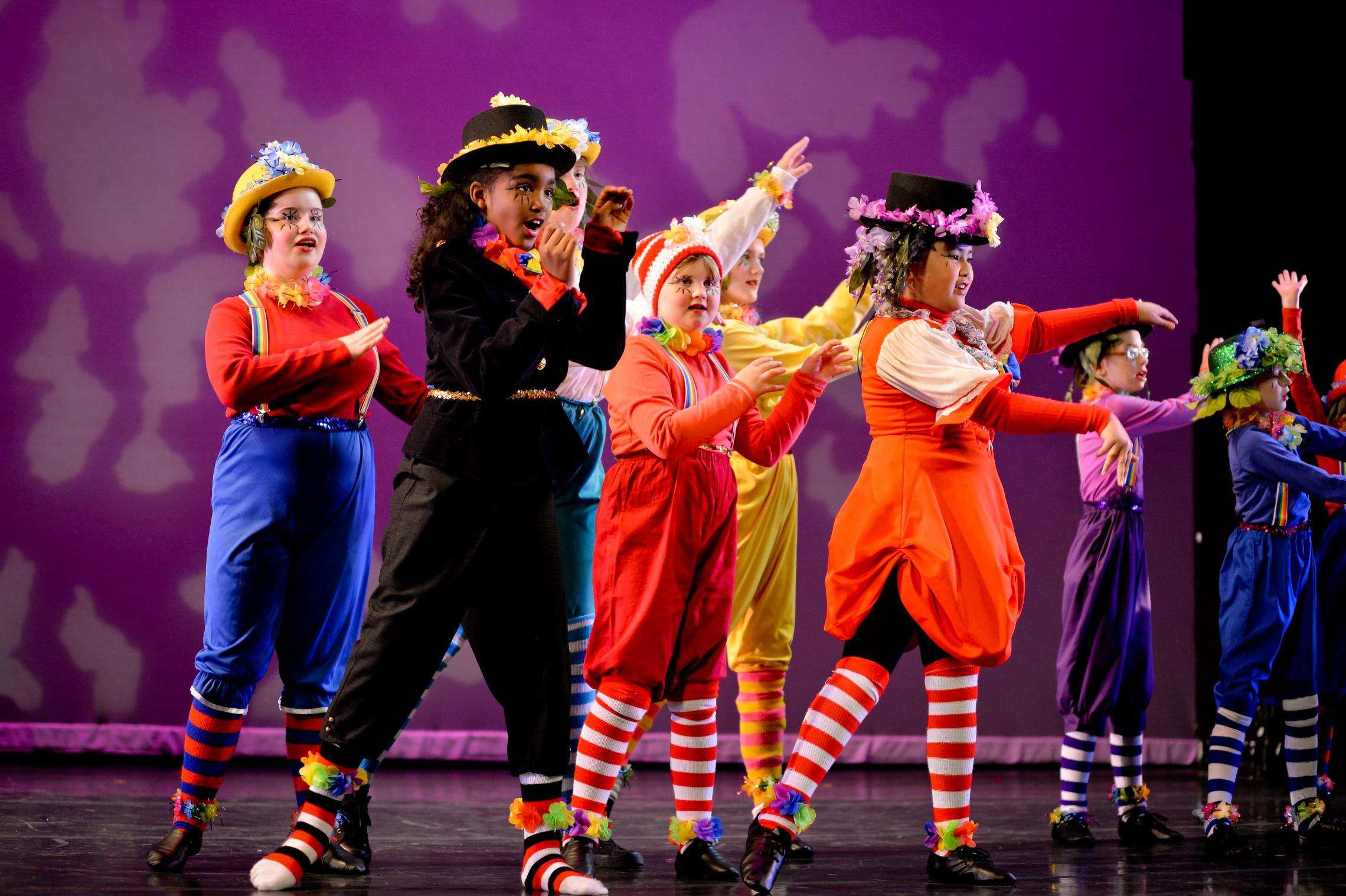 Children participate in a YMCA youth theatre performance, wearing colorful costumes and performing on stage during an arts program recital in Pierce and Kitsap counties.
