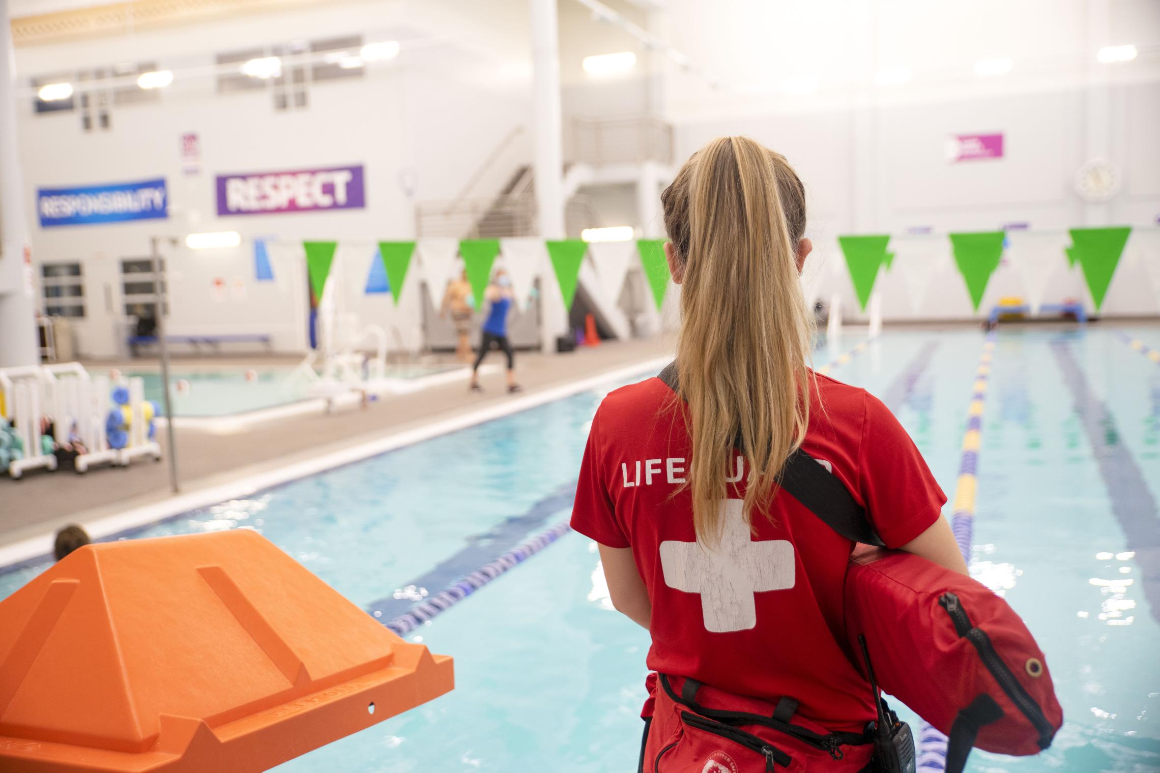 YMCA lifeguard standing beside an indoor swimming pool in Pierce and Kitsap Counties, promoting water safety, swim lessons, and summer family wellness.