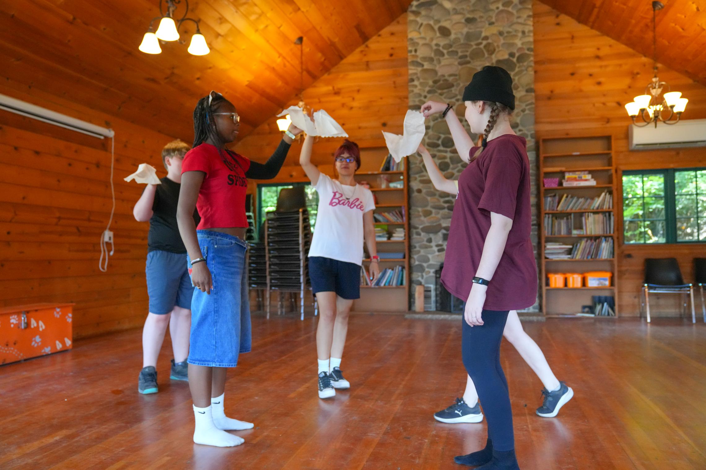 YMCA Kosovo counselors Erza and Riga teach campers a traditional Albanian handkerchief dance inside a Camp Seymour lodge, sharing cultural traditions through music, movement, and group participation.