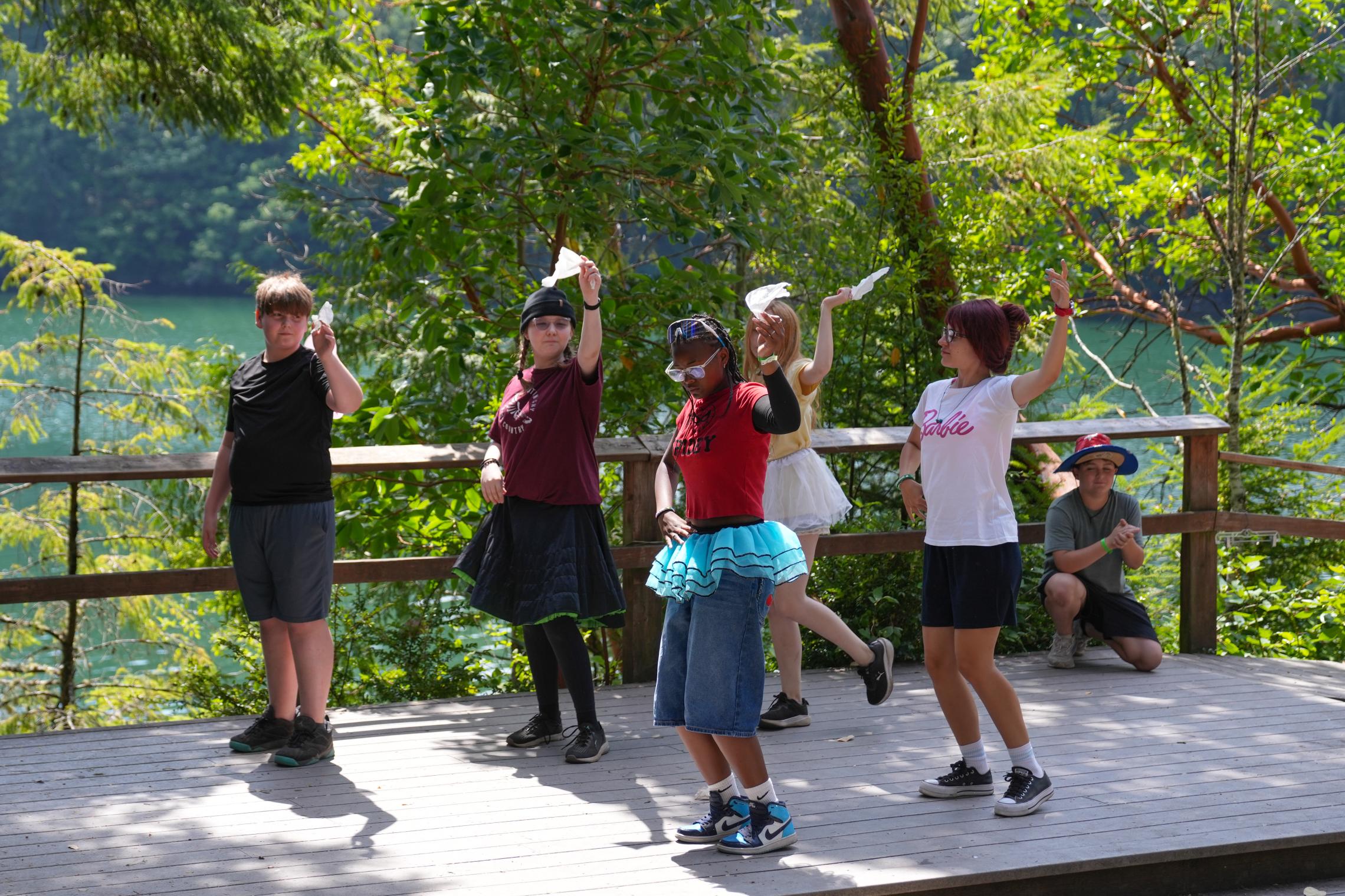 Camp Seymour campers and YMCA Kosovo counselor Erza perform a traditional Albanian handkerchief dance on an outdoor stage overlooking the waterfront, sharing culture and global connections through camp activities.