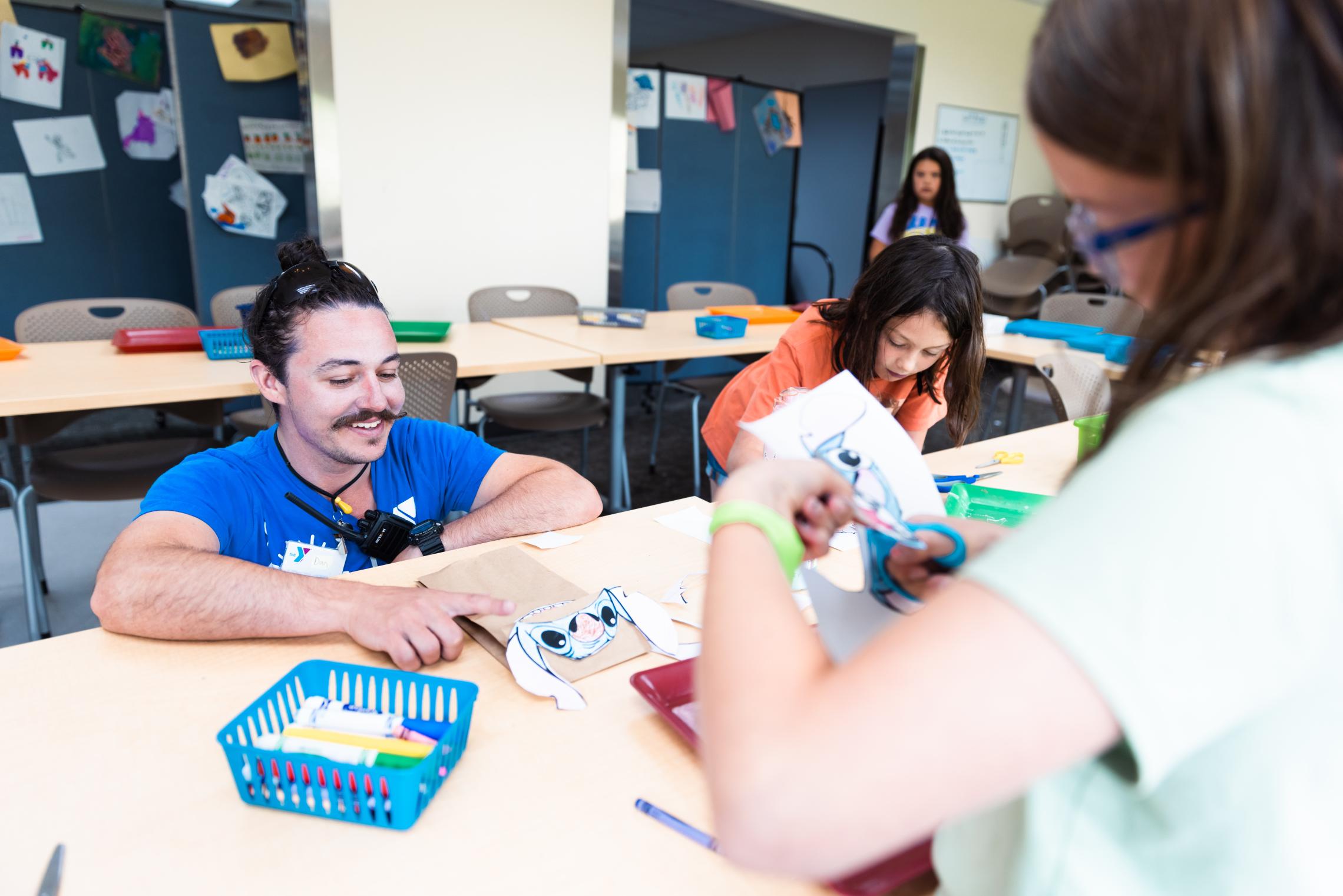 YMCA arts instructor helps children with a visual arts project during a creative learning class at a YMCA arts program in Pierce and Kitsap Counties.