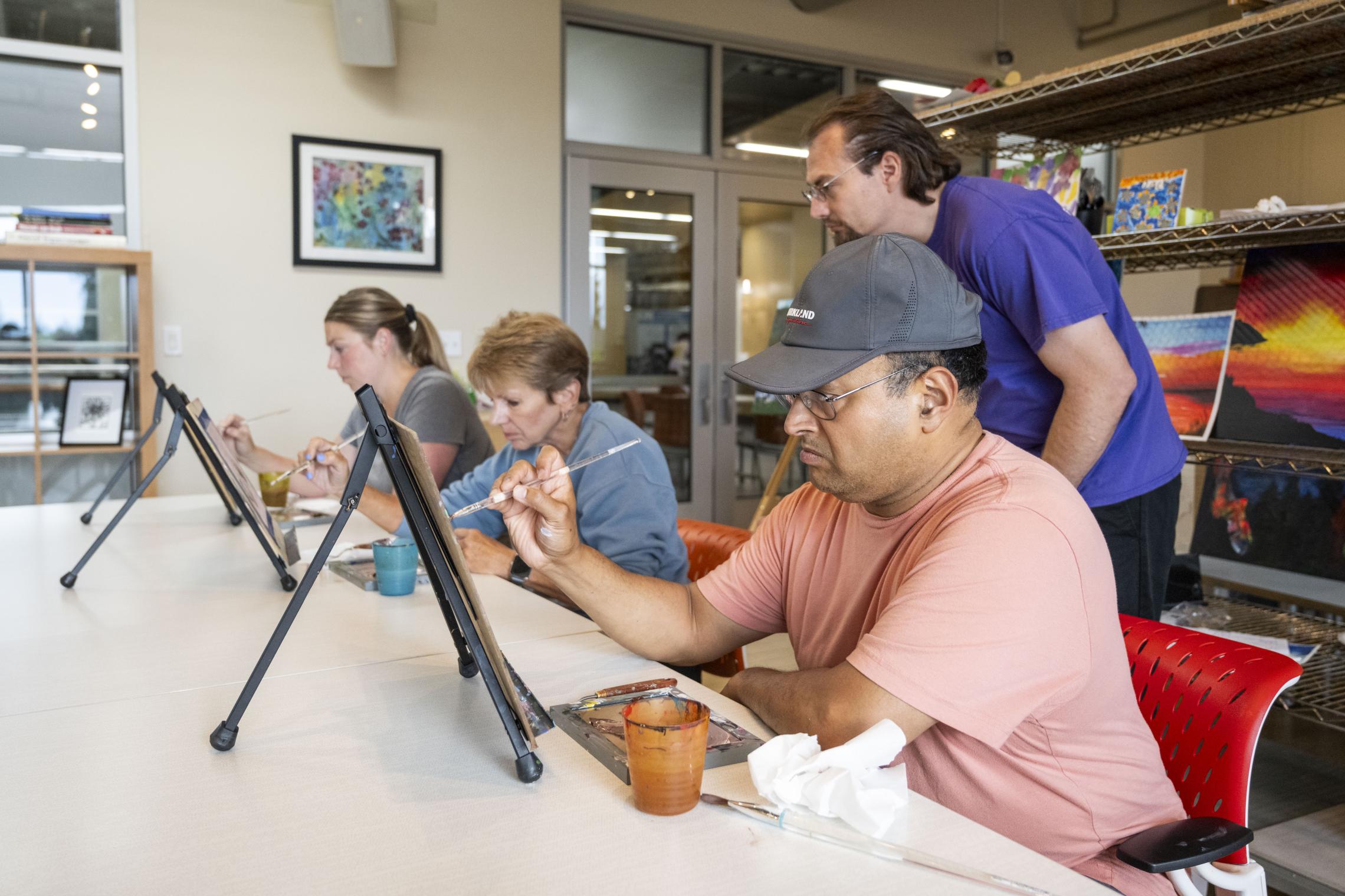Adults participate in a YMCA visual arts class, painting on canvases while receiving instruction in a community-based arts education program.
