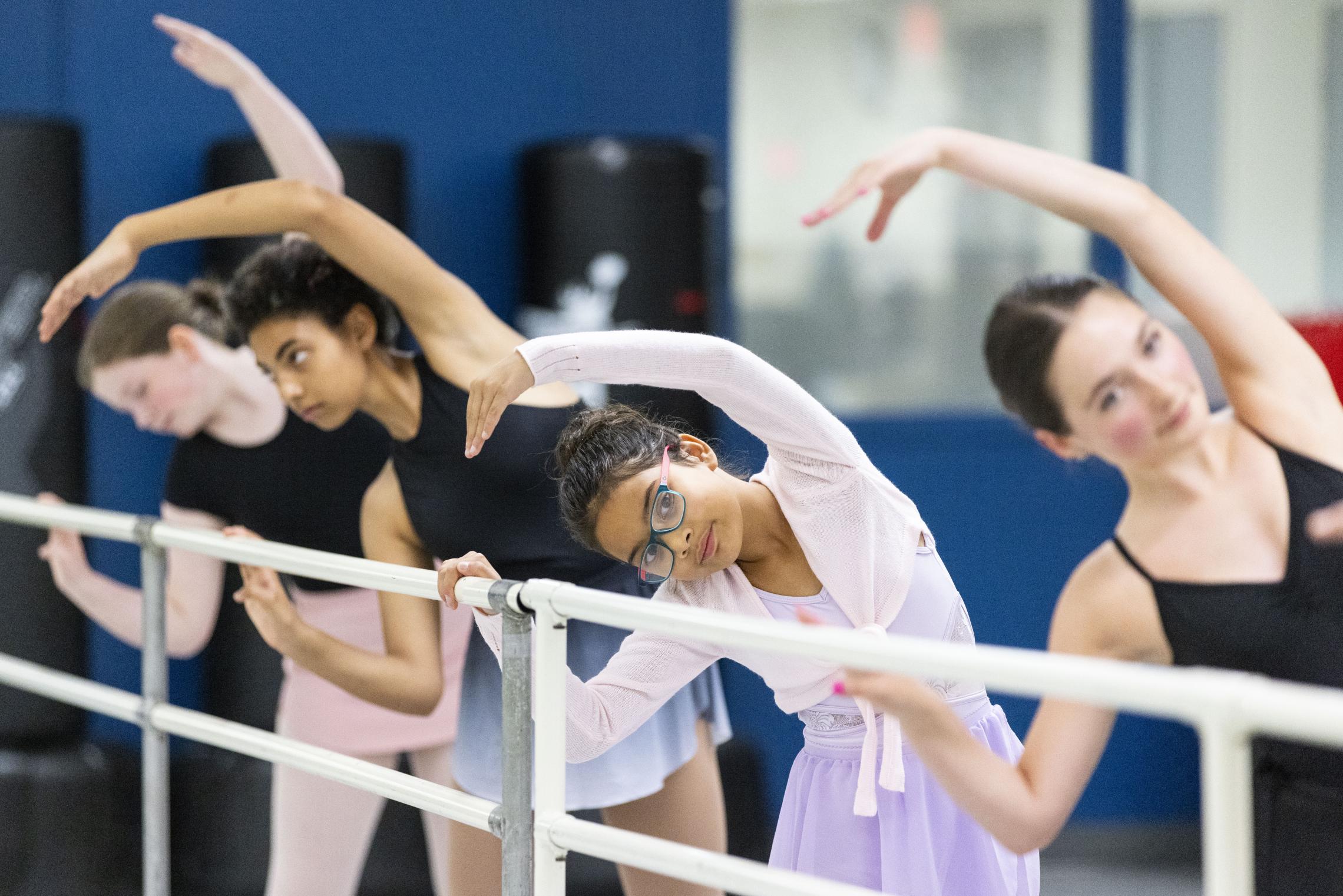 Children and youth participate in a YMCA ballet class, practicing stretches at a barre during a community arts and dance program in Pierce and Kitsap Counties.