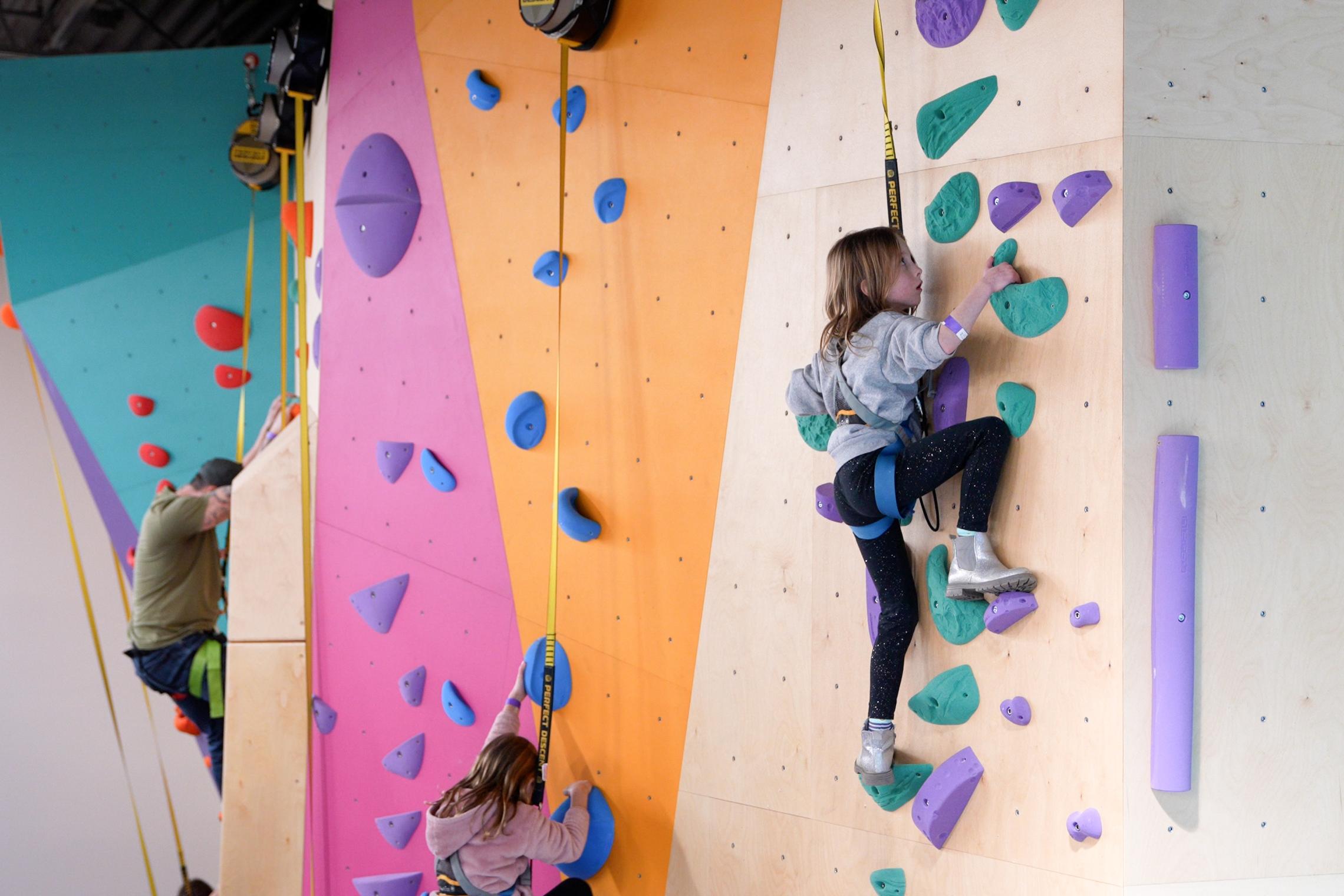 Children climb the Liz Rocks Climbing Wall at the Pearl Street Family YMCA, building confidence, strength, and teamwork through youth adventure programs.