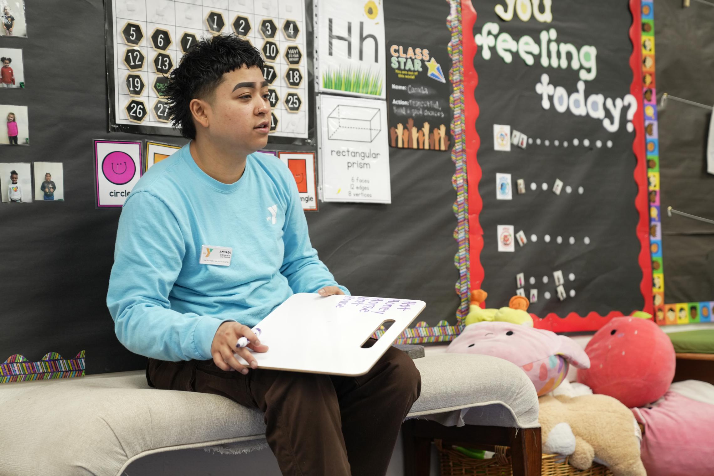 An early learning educator reads a picture book to a group of children gathered on a classroom rug during story time. Children sit closely around the educator in a bright early learning classroom, listening and looking at the book.