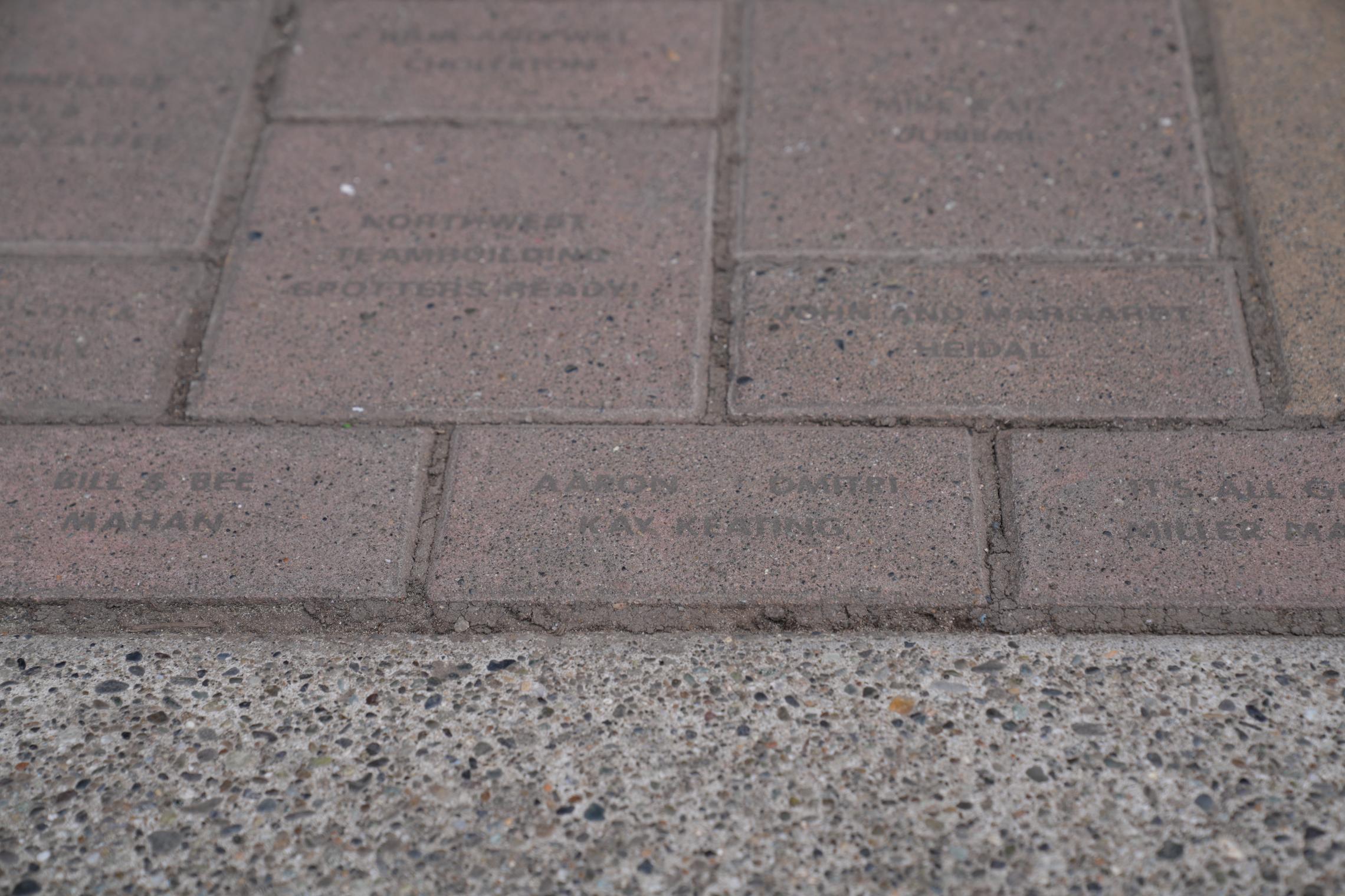 An engraved brick walkway at Camp Seymour features personalized donor bricks, including one bearing the Keating family name. The close-up photo shows several commemorative bricks set into a paved path beside a concrete edge.