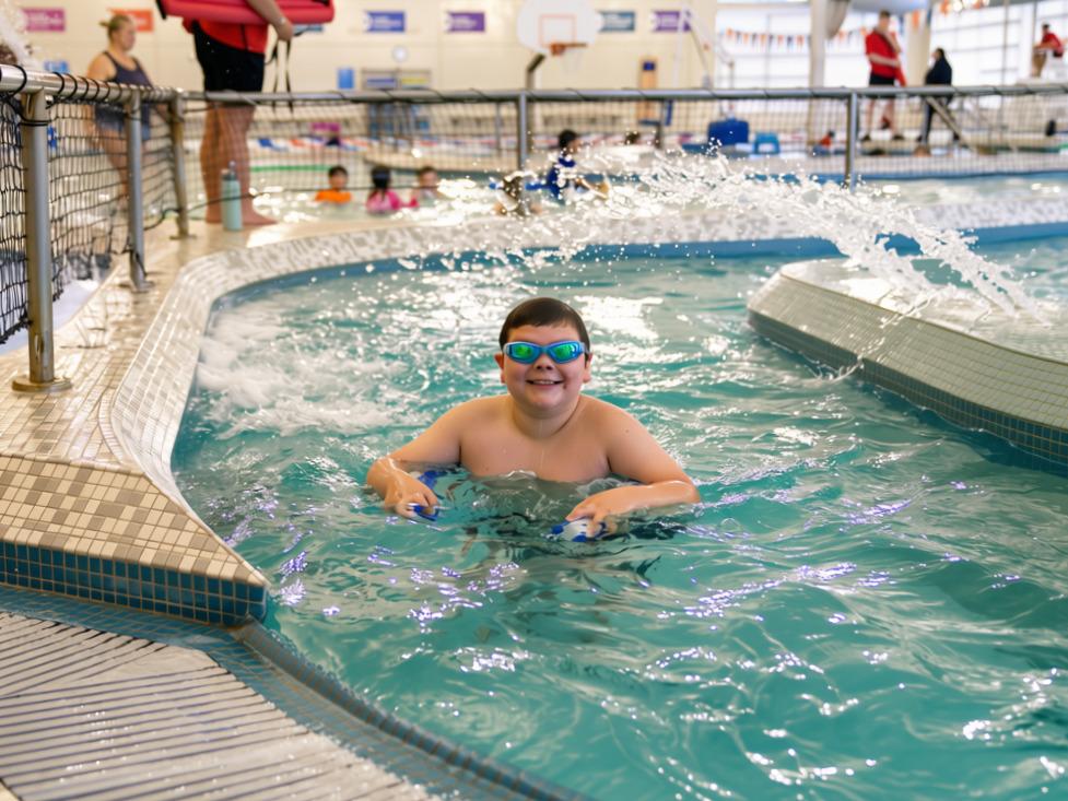 Beary swims in the lazy river at the Gordon Family YMCA aquatic center while wearing swim goggles during a YMCA swim lesson.