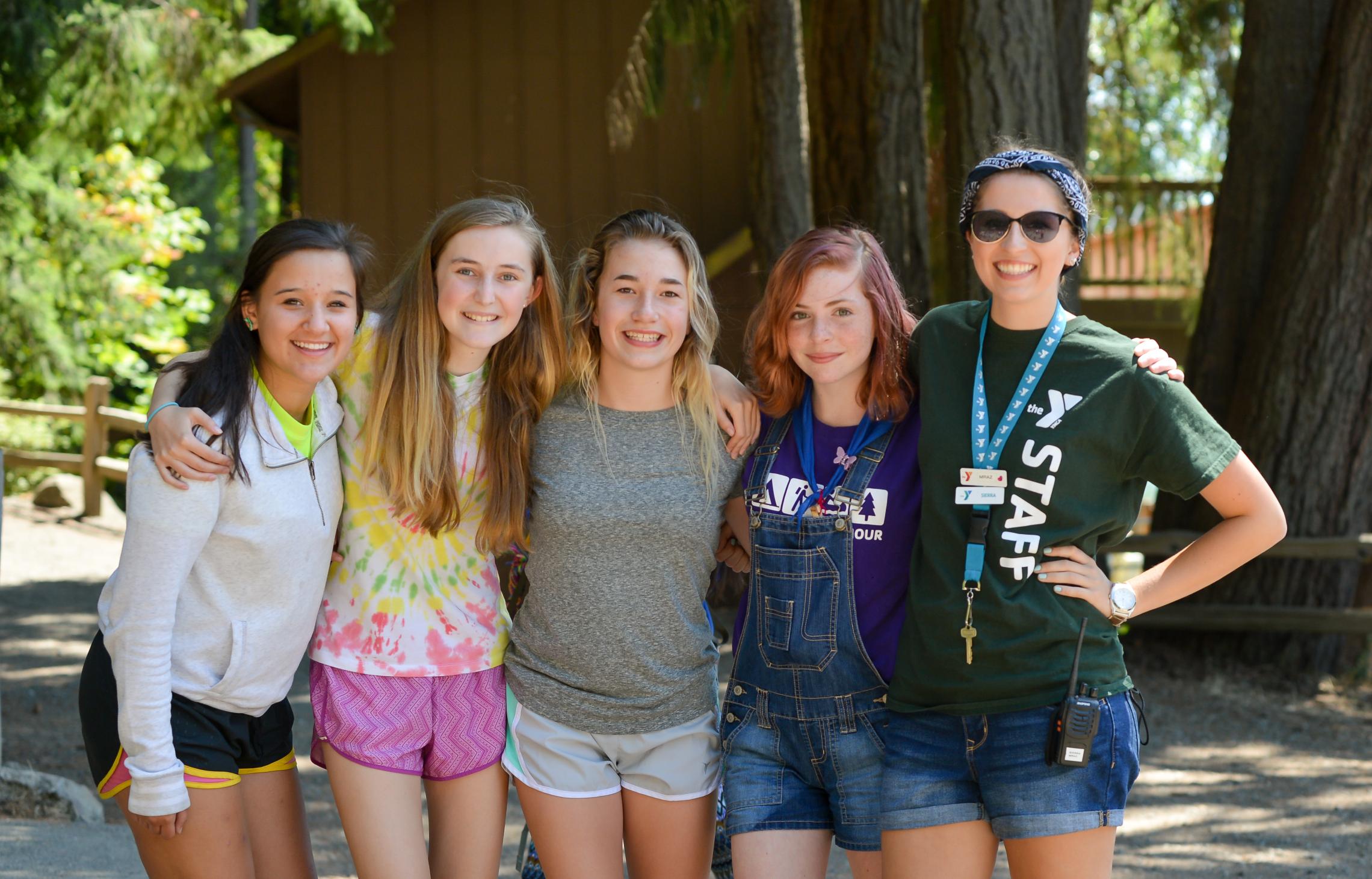 Camp Seymour staff member stands with four teen participants outdoors at YMCA Camp Seymour, highlighting the camp's leadership development pathway from camper to counselor.