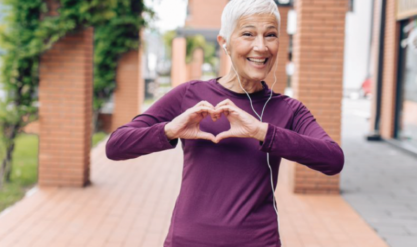 Active older woman making a heart shape with her hands and wearing a big smile.