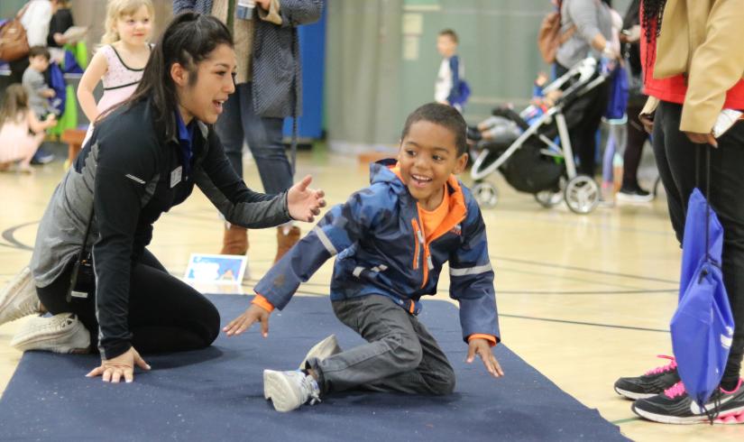 Young boy tumbles on a mat with a YMCA staff member cheering them on.