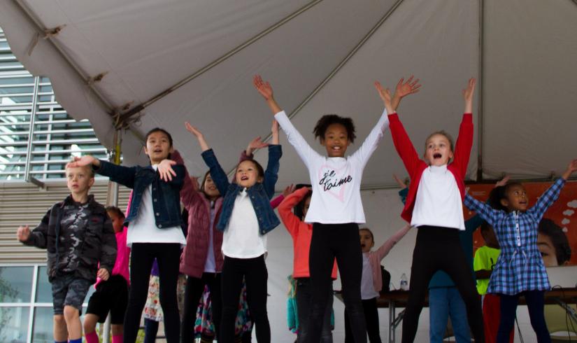 A group of 12 kids have their arms outstretched in a Y shape on stage at a Y event.