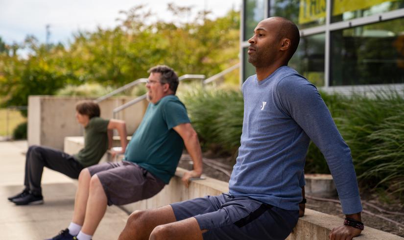 An African American man in a blue Y shirt leads two men in an outdoor boot camp.