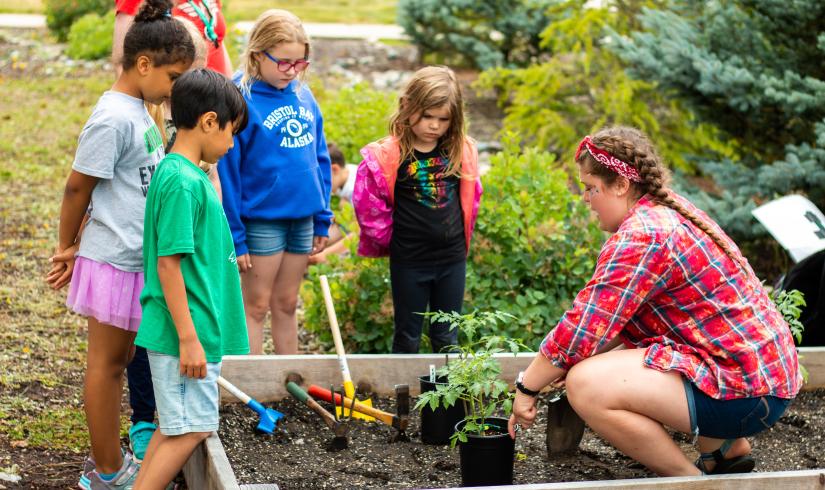 Children and an instructor gather around a planter box.