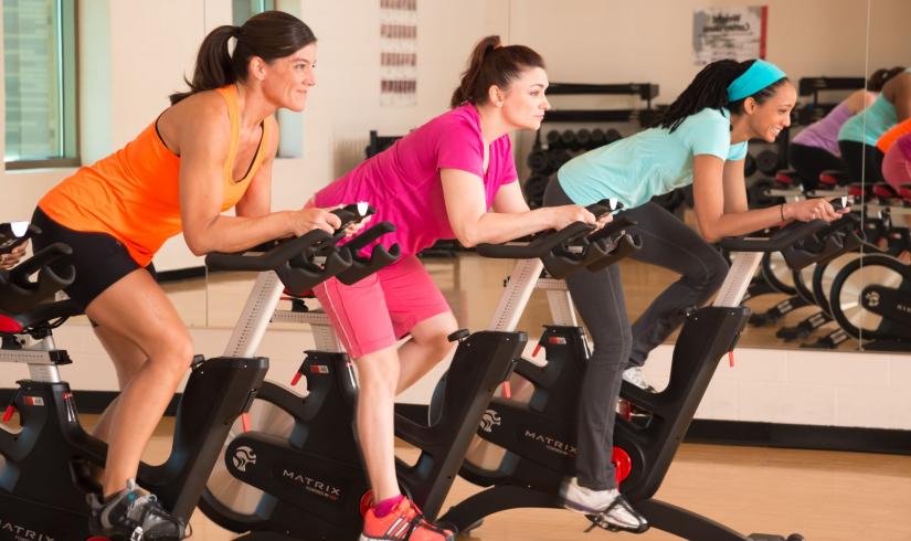 Three women on stationary bikes enjoy a group exercise class