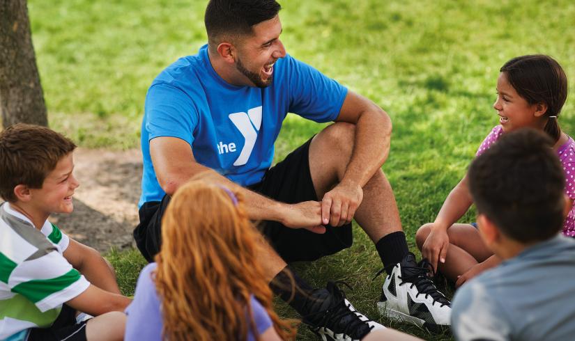 A camp counselor sits with a group of children at the Y