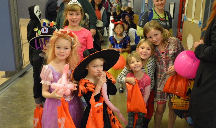 Groups of children trick-or-treat at the YMCA as witches, princesses, ghosts and more. They are smiling and holding bags of candy!