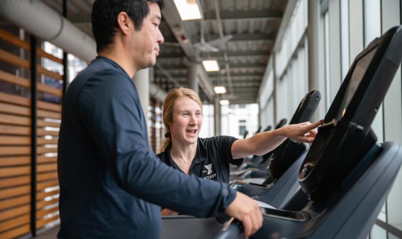 Wellness Coach Becca provides an equipment orientation on a treadmill to a member.