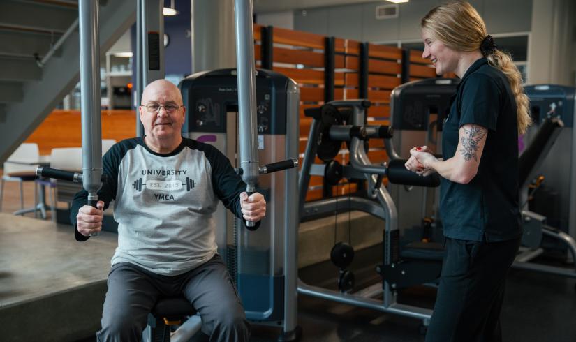 Wellness Coach Becca provides guidance to a member using an upper body piece of equipment.