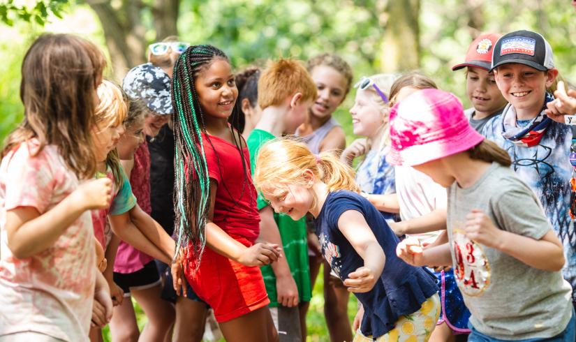 A group of kids dressed in different shades of t-shirts and shorts are laughing, smiling, and having fun.