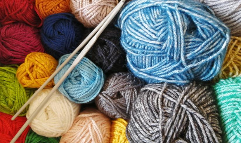 Balls of colorful yarn are viewed from above along with a set of knitting needles.