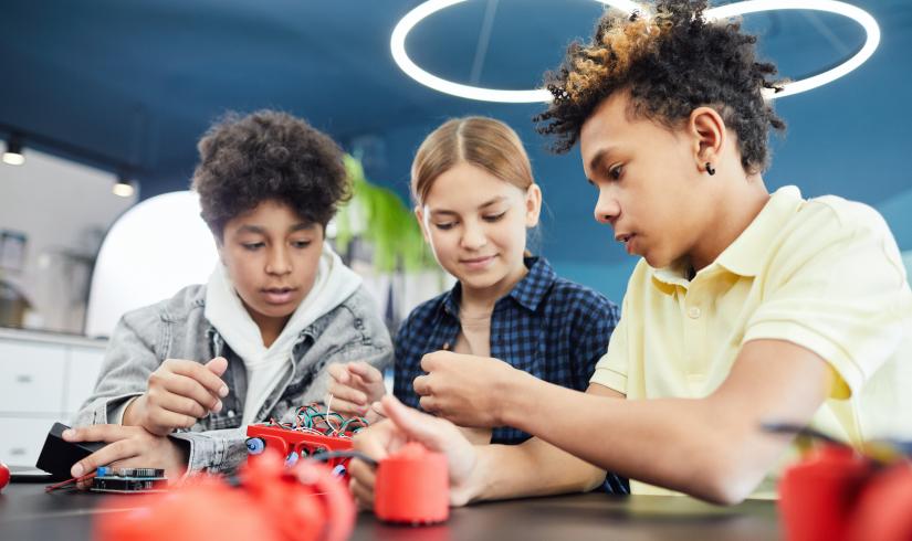 Three pre-teens collaborate together on a robotics project. 