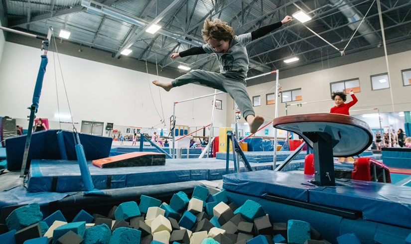 A young boy does a split and screams with excitement after jumping into a foam block pit in the gymnastics center.