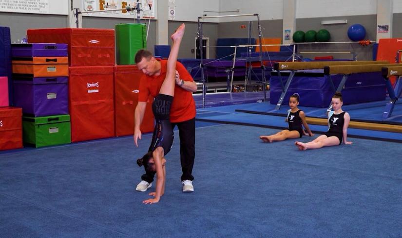 Gymnastics instructor supports a gymnast's position in a handstand and helps align their body.