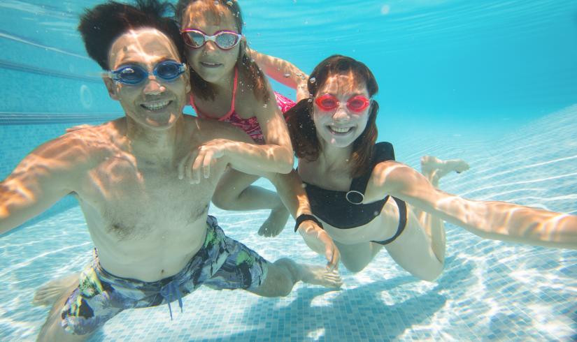 An Asian American man swims underwater with two daughters in a Y pool.
