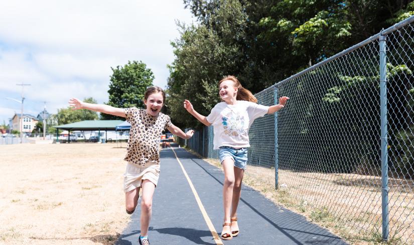 Two summer camp participants skipping down the outdoor track at the YMCA