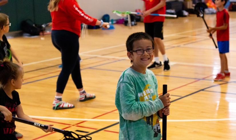 Summer camp participant posing with a lacrosse stick at the YMCA