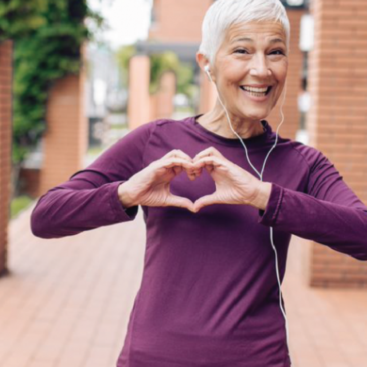 Active older woman making a heart shape with her hands and wearing a big smile.