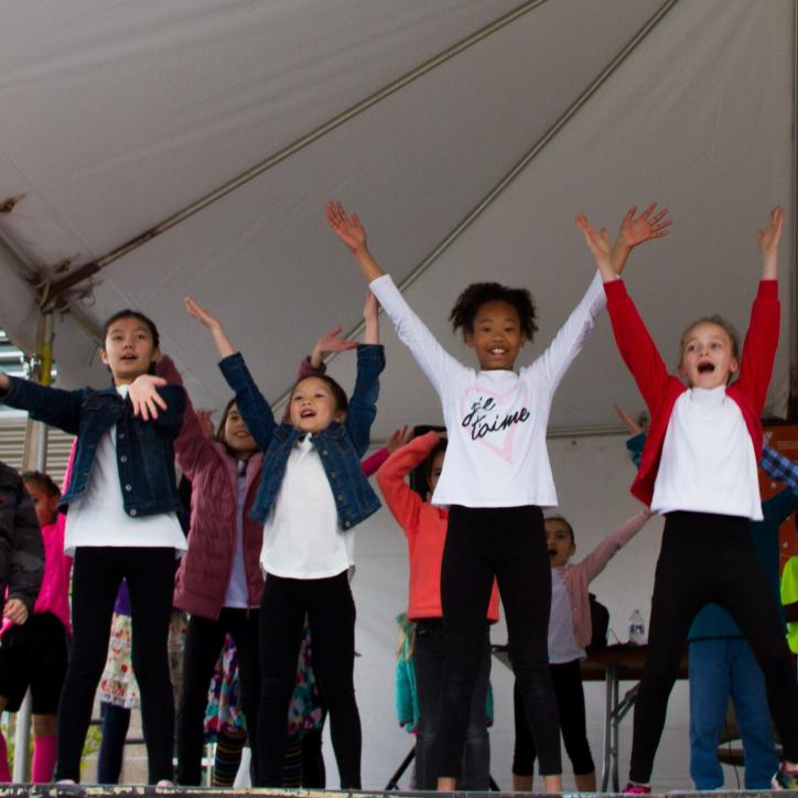 A group of 12 kids have their arms outstretched in a Y shape on stage at a Y event.