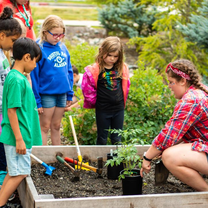 Children and an instructor gather around a planter box.