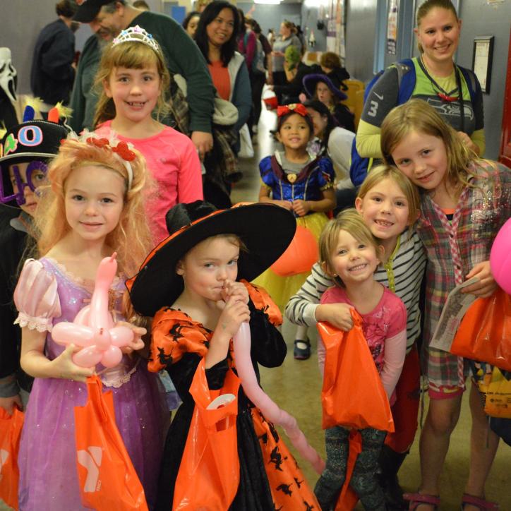 Groups of children trick-or-treat at the YMCA as witches, princesses, ghosts and more. They are smiling and holding bags of candy!