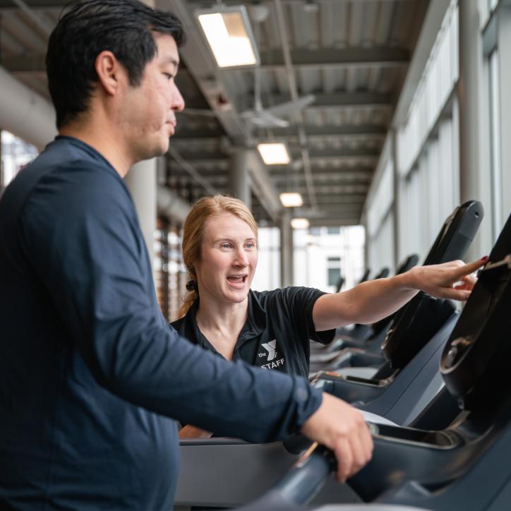 Wellness Coach Becca provides an equipment orientation on a treadmill to a member.
