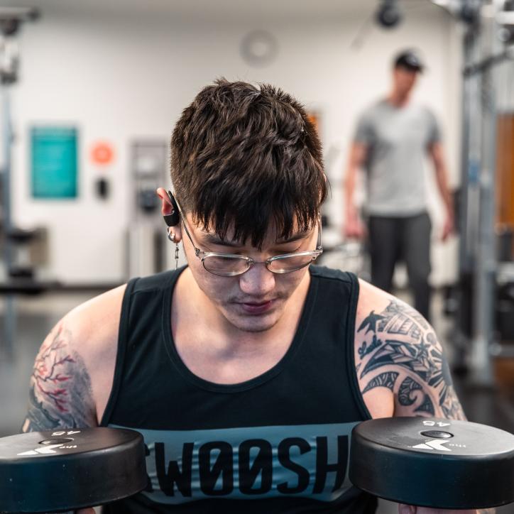 A young Asian American man reflects and holds two 45 pound free weights at the University YMCA Student Center.