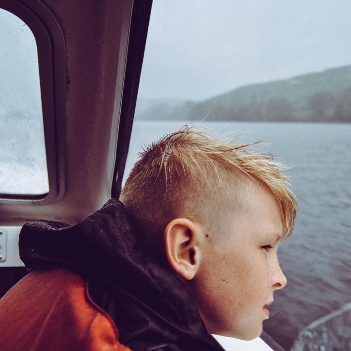 A young boy looks out over the water on a gray day. His eyes are off camera centered on what's beyond the frame.