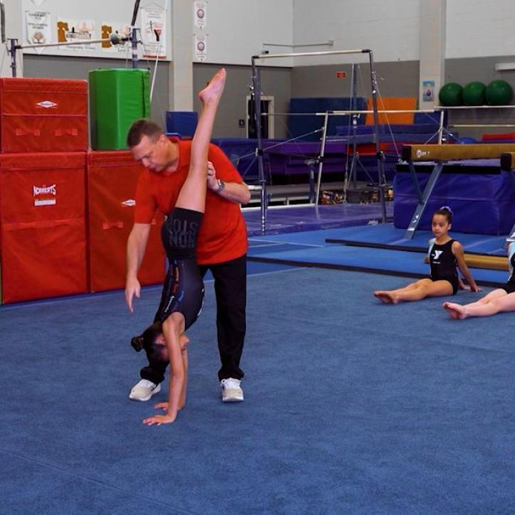 Gymnastics instructor supports a gymnast's position in a handstand and helps align their body.