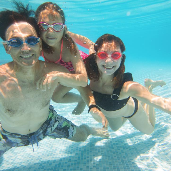 An Asian American man swims underwater with two daughters in a Y pool.