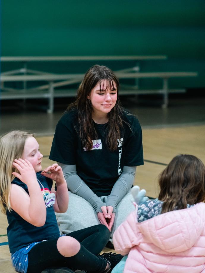 Teen leader crouches to speak with kids night out participants