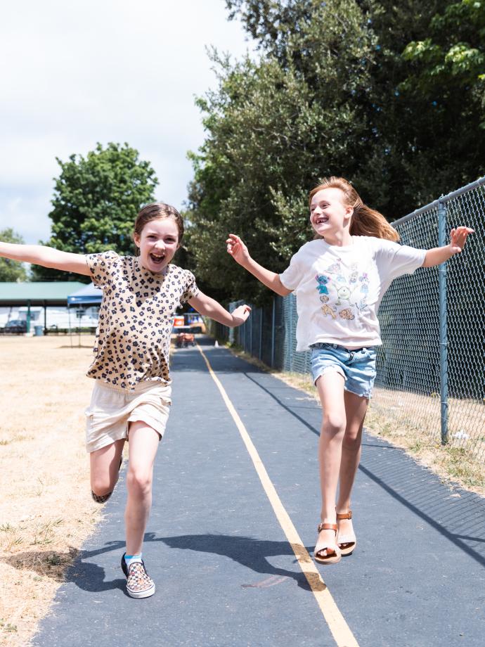 Two summer camp participants skipping down the outdoor track at the YMCA